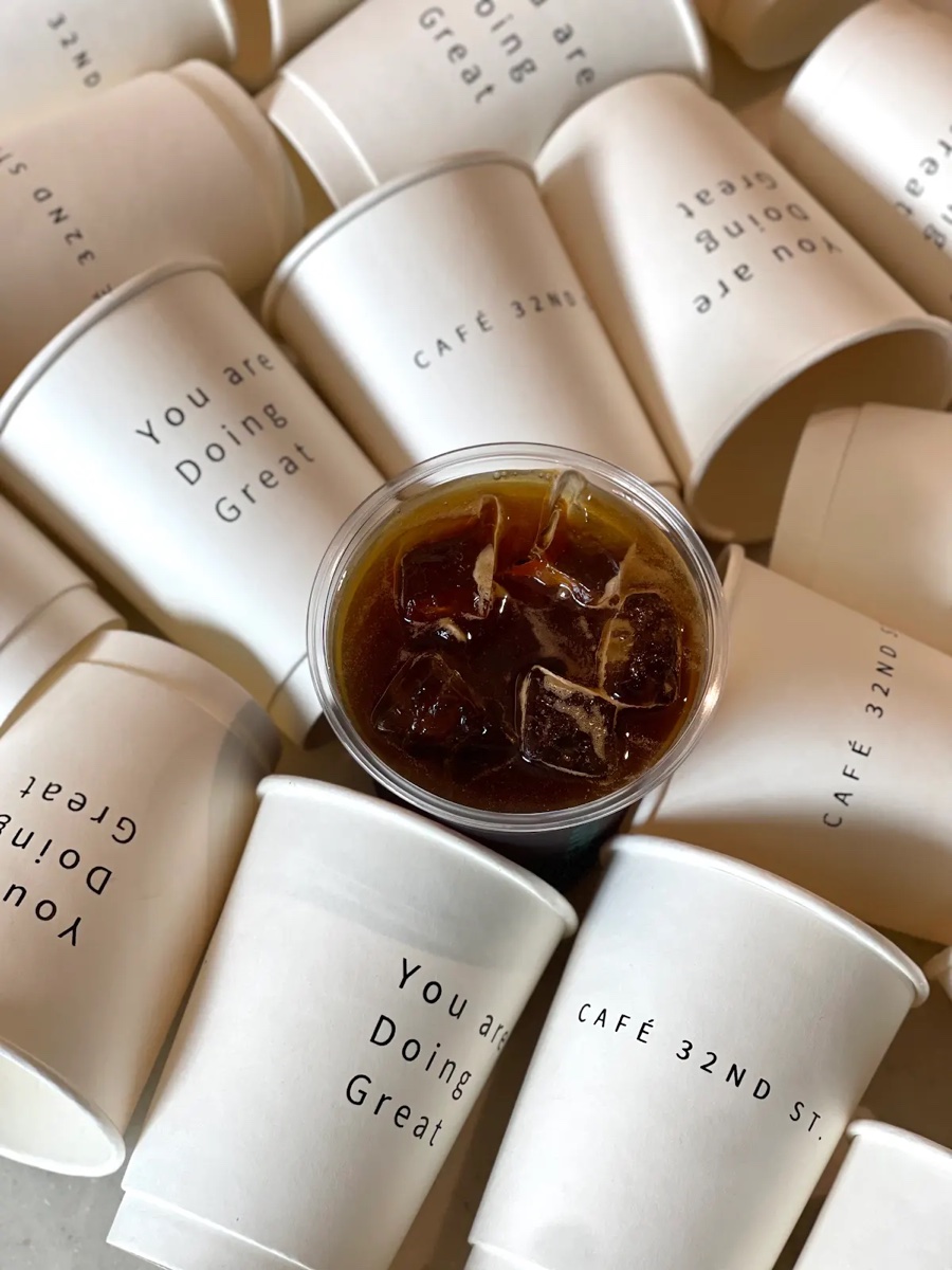 Iced coffee nestled among a pile of 'You are Doing Great' branded Cafe 32nd St cups