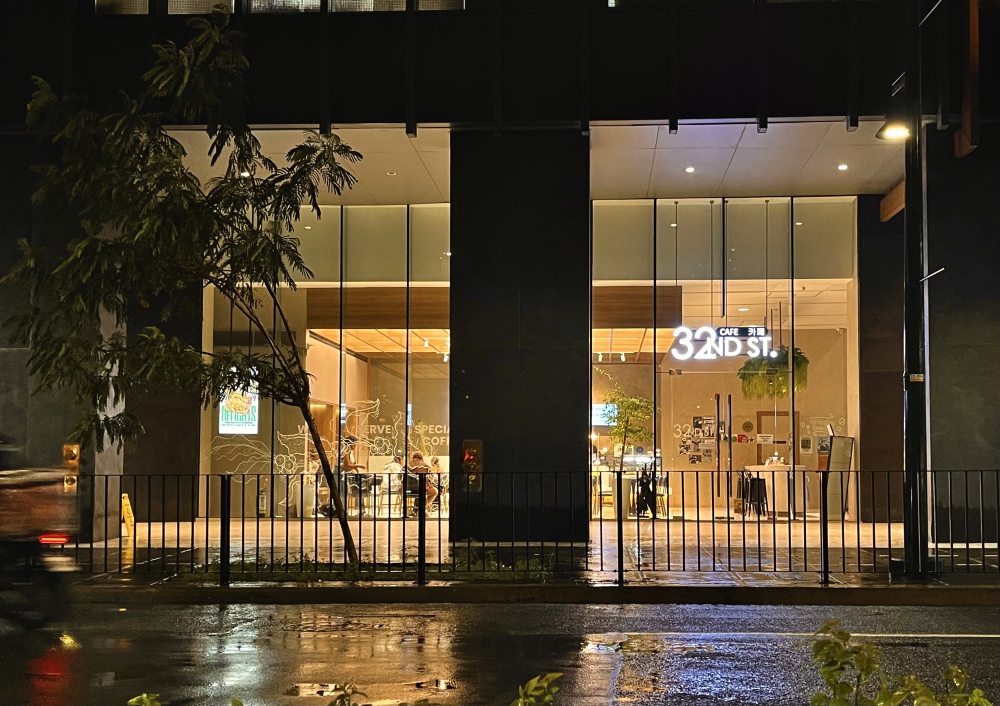 Cafe 32nd St storefront glowing at night, seen from across 32nd Street in BGC