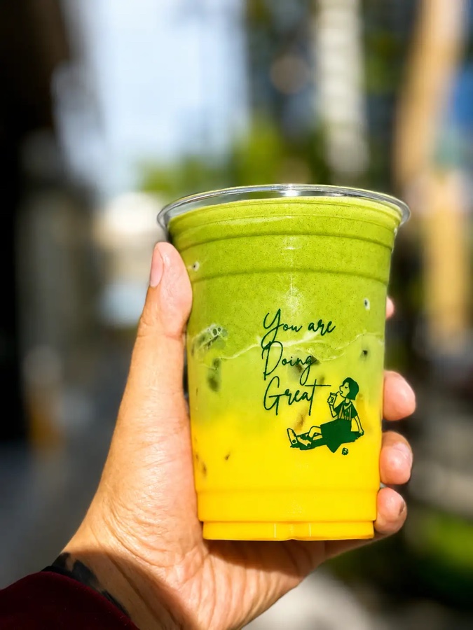 A hand holding an iced matcha strawberry drink from Cafe 32nd St outdoors